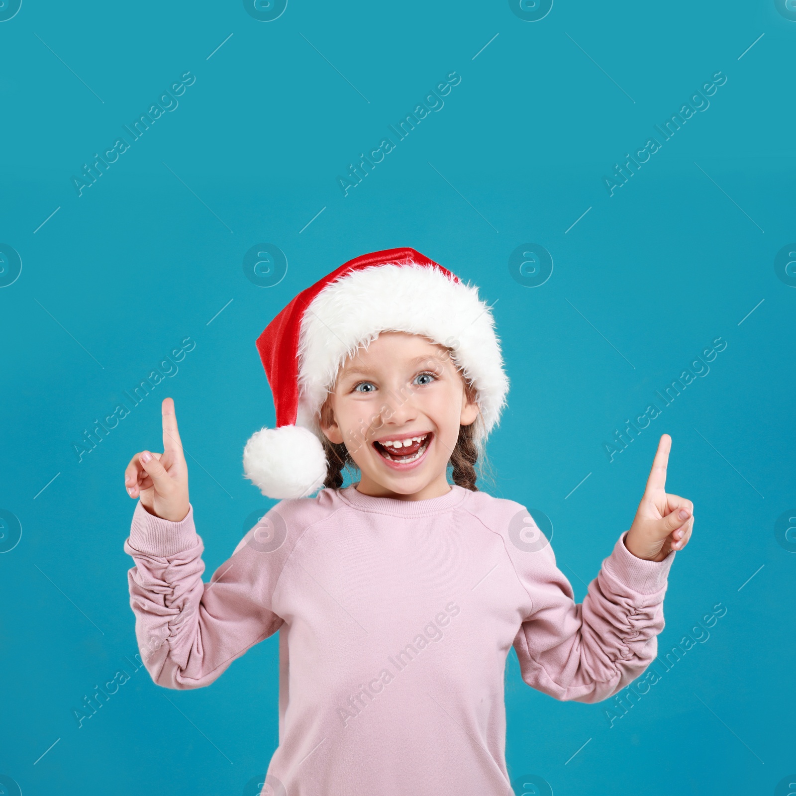 Image of Happy little child in Santa hat on light blue background. Christmas celebration