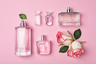 Bottles of perfume and roses on color background, top view