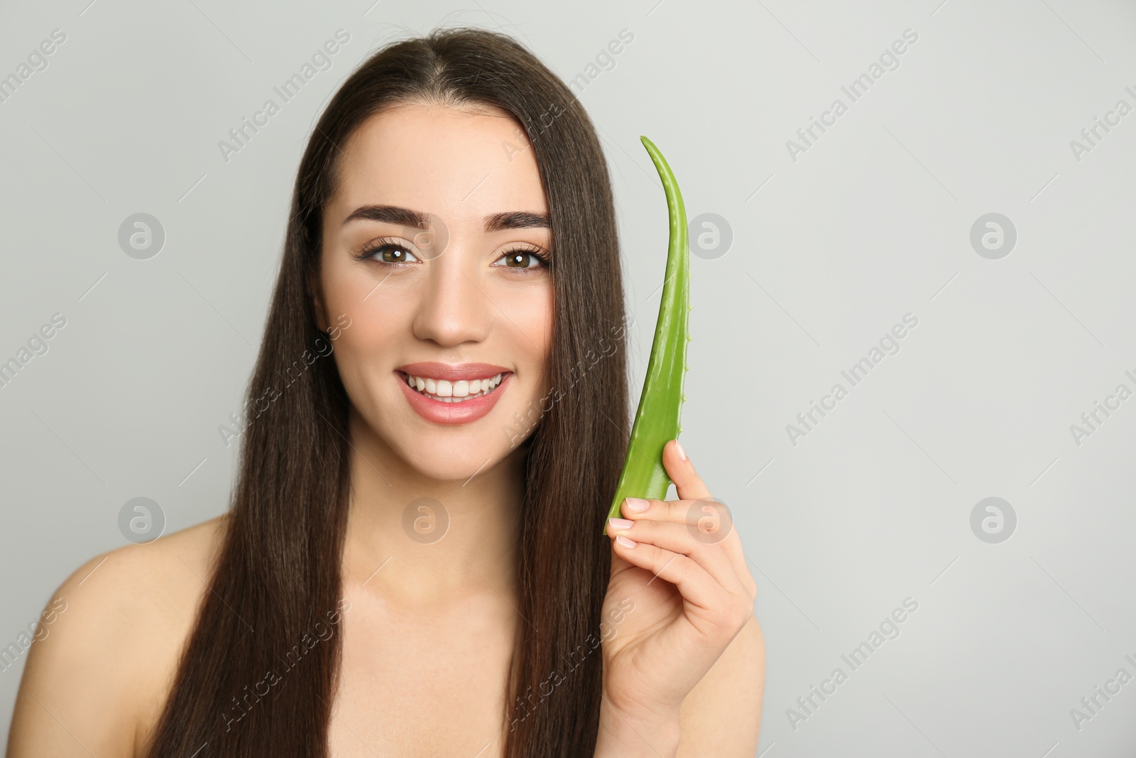 Photo of Young woman with aloe vera leaf on light grey background. Space for text