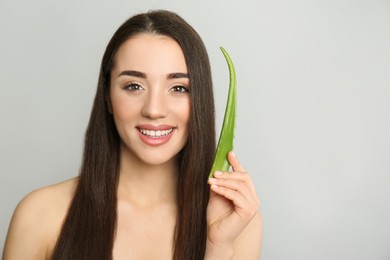 Photo of Young woman with aloe vera leaf on light grey background. Space for text