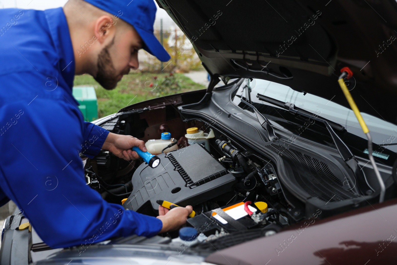 Photo of Young mechanic with flashlight fixing car outdoors