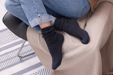 Photo of Woman in warm socks sitting on armchair at home, closeup