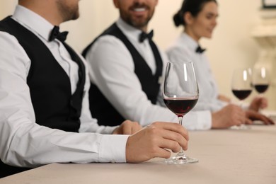 Photo of People with glasses of red wine at table indoors, closeup. Professional butler courses