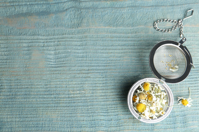 Photo of Dry chamomile flowers in infuser on light blue wooden table, flat lay. Space for text