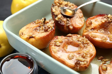 Tasty baked quinces with nuts and honey in dish on grid, closeup