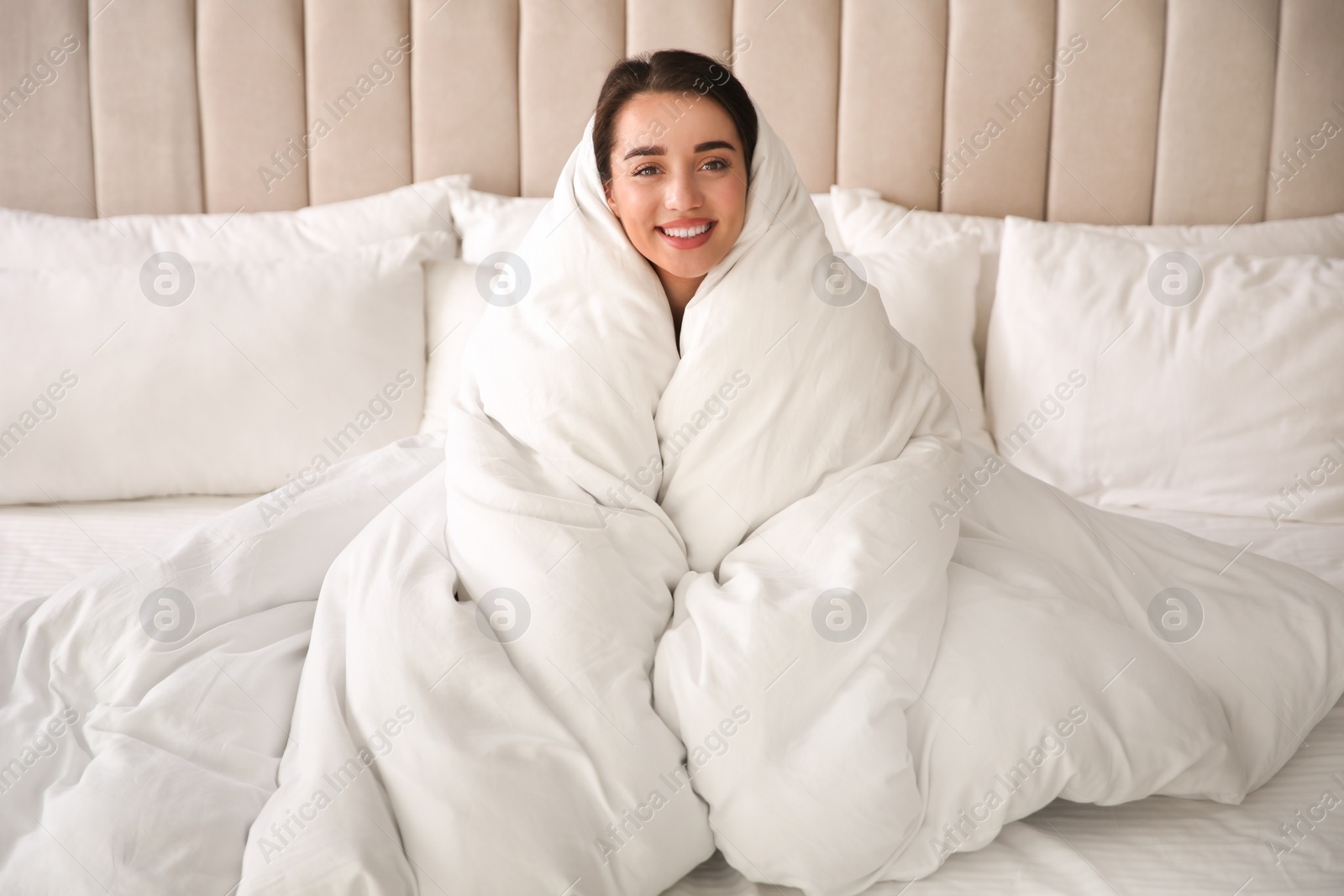 Photo of Beautiful young woman wrapped with soft blanket relaxing on bed at home