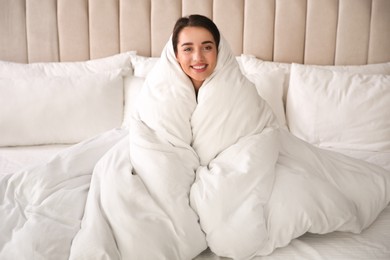 Photo of Beautiful young woman wrapped with soft blanket relaxing on bed at home