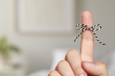 Photo of Man showing index finger with tied bow as reminder on blurred background, closeup. Space for text