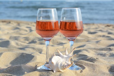 Glasses of tasty rose wine and seashell on sand near sea