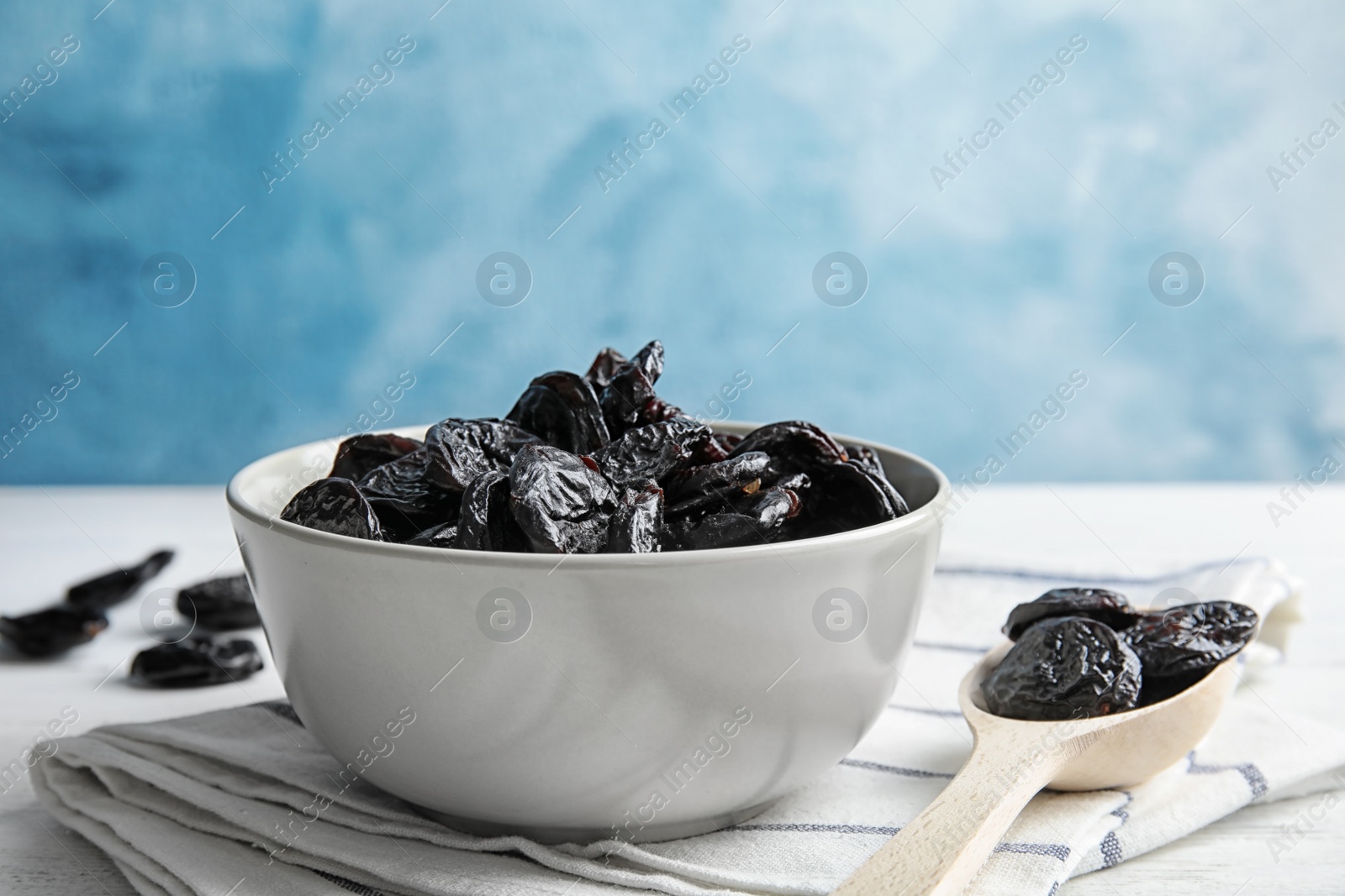 Photo of Bowl and spoon of sweet dried plums on table. Healthy fruit