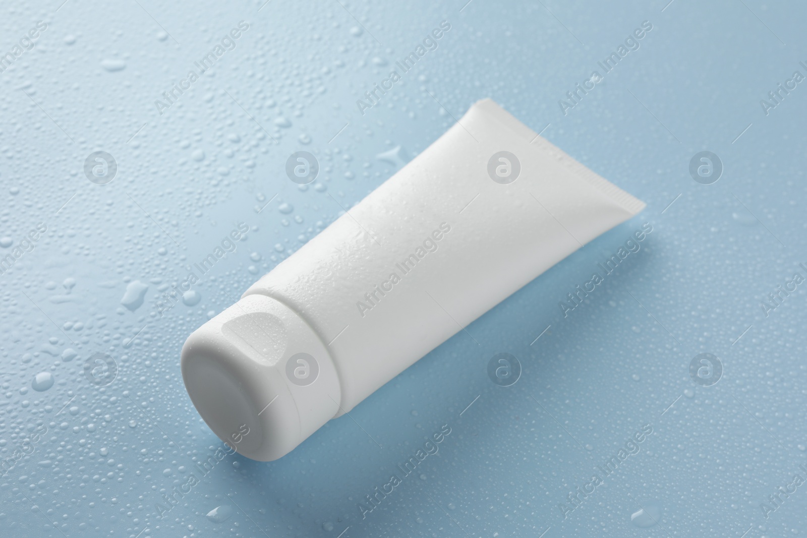 Photo of Moisturizing cream in tube on light blue background with water drops, closeup