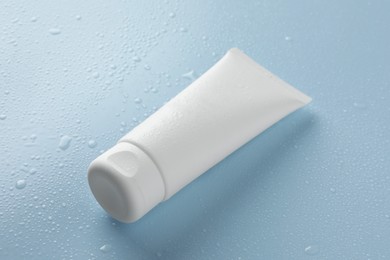 Photo of Moisturizing cream in tube on light blue background with water drops, closeup
