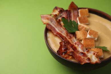 Photo of Delicious lentil soup with bacon and parsley in bowl on green table, closeup. Space for text