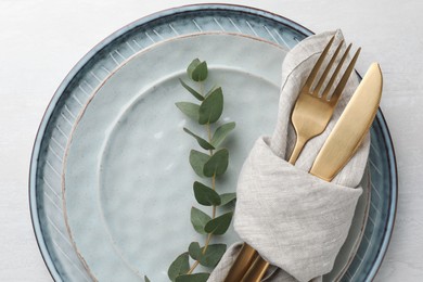 Stylish setting with cutlery, napkin, eucalyptus branch and plates on white table, top view