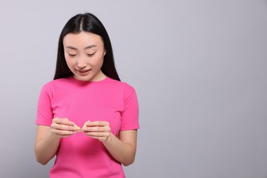 Photo of Asian woman breaking tasty fortune cookie with prediction on grey background, space for text