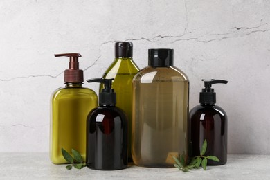 Shampoo bottles and leaves on light grey table