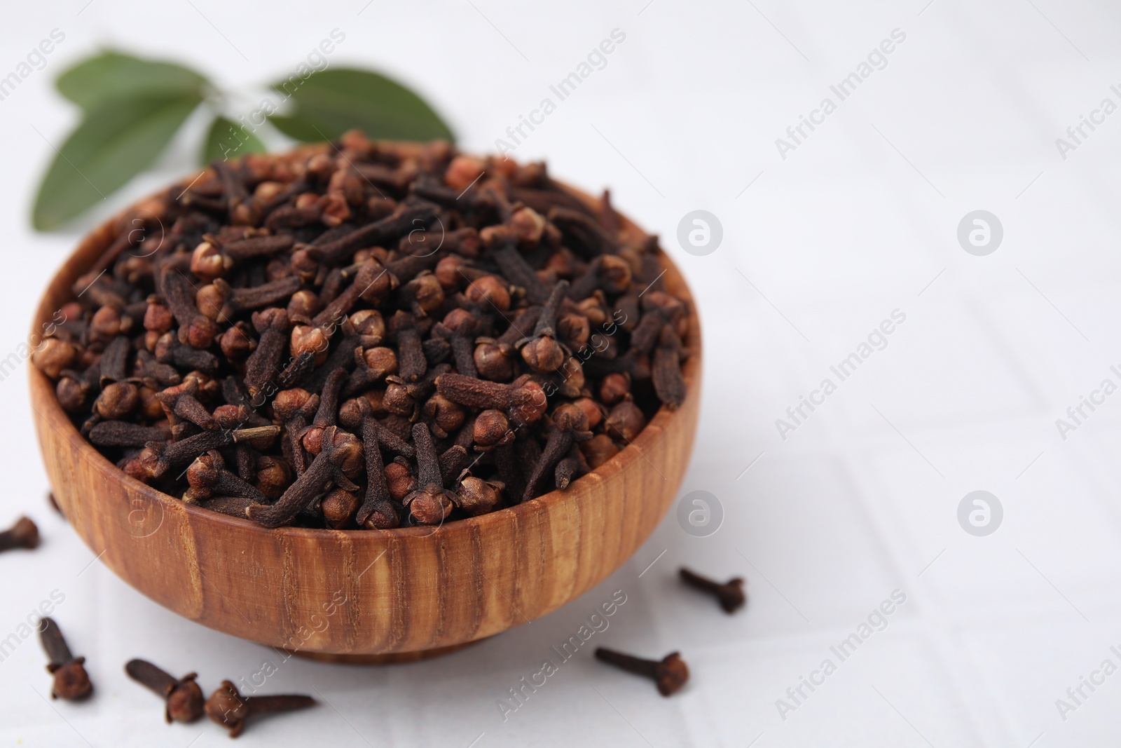 Photo of Aromatic cloves in bowl on white tiled table, closeup. Space for text