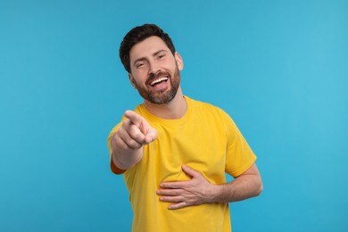 Photo of Handsome man pointing at something and laughing on light blue background