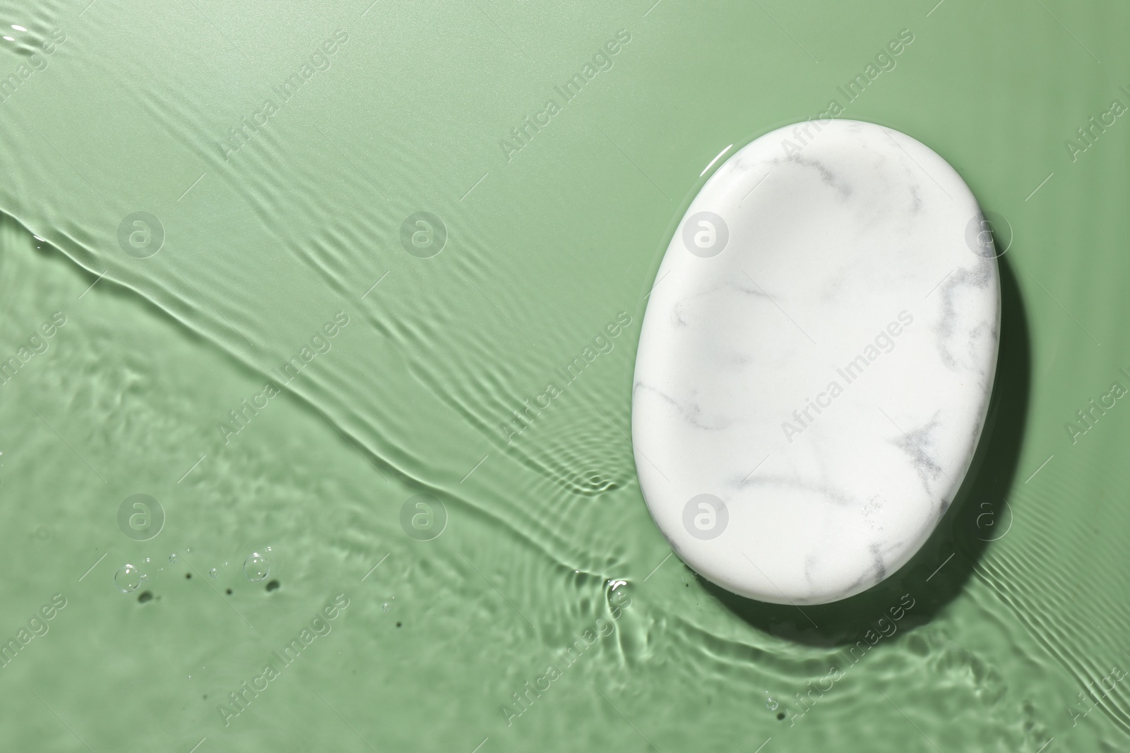 Photo of Presentation of product. Marble podium in water on green background, top view. Space for text