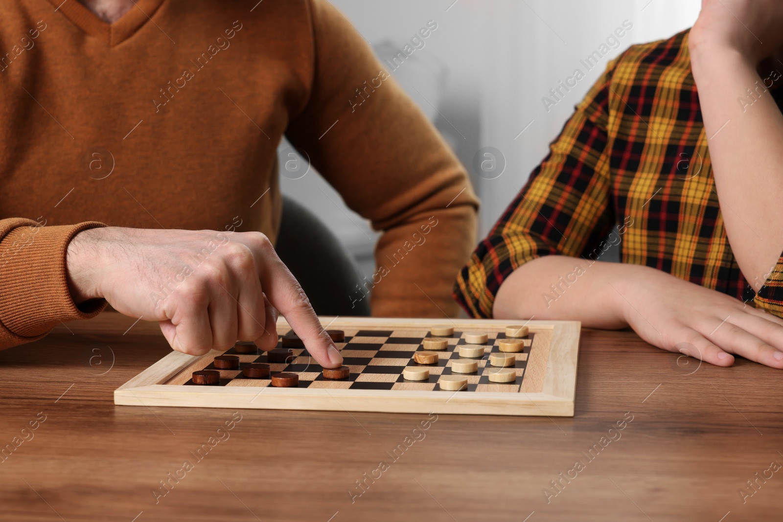 Photo of Father playing checkers with his son at table in room, closeup