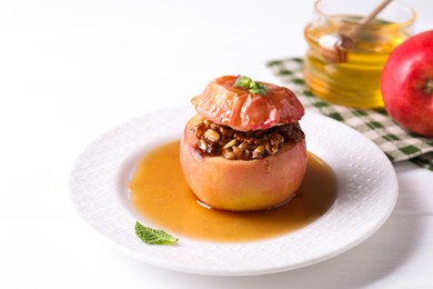 Photo of Tasty baked apple with nuts, honey and mint on white table, closeup