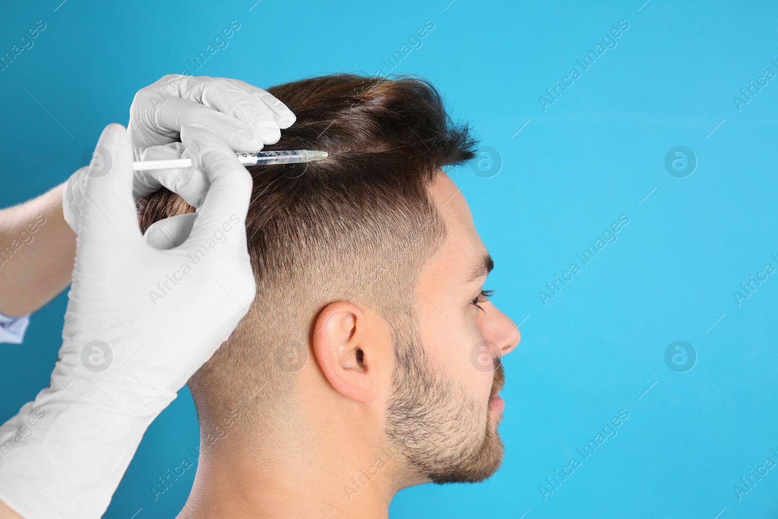 Photo of Young man with hair loss problem receiving injection on color background