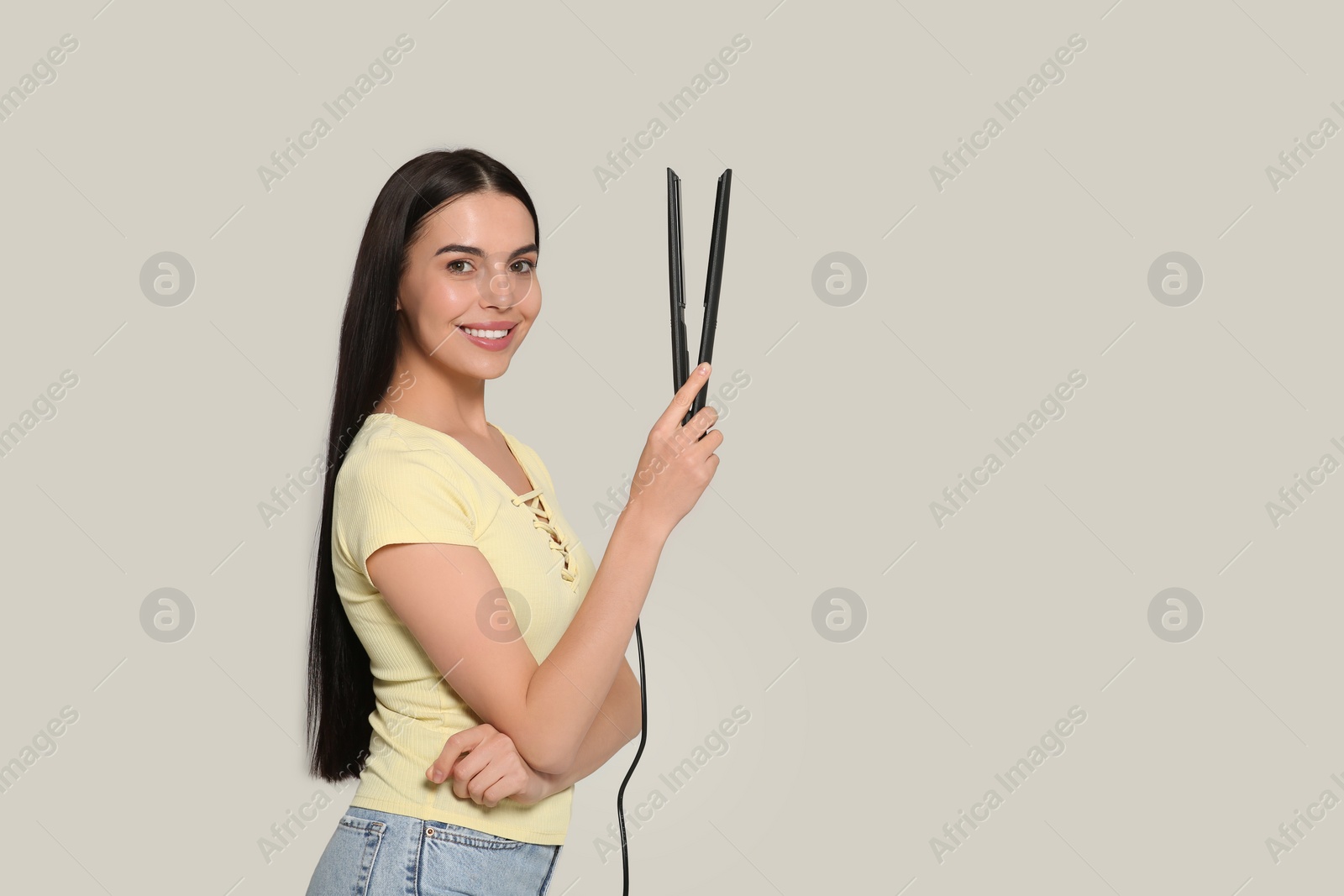 Photo of Beautiful happy woman with hair iron on light grey background. Space for text