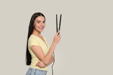 Beautiful happy woman with hair iron on light grey background. Space for text