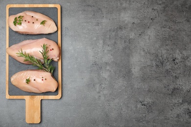 Photo of Board with raw chicken meat and spices on grey background, top view. Space for text