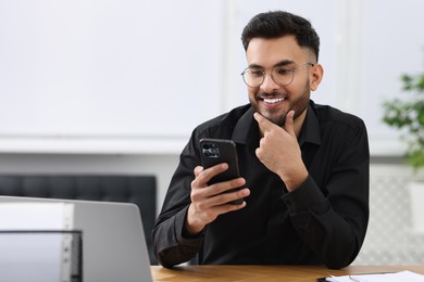 Handsome young man using smartphone at wooden table in office