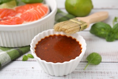 Photo of Fresh marinade, fish, brush and basil on white wooden table, closeup