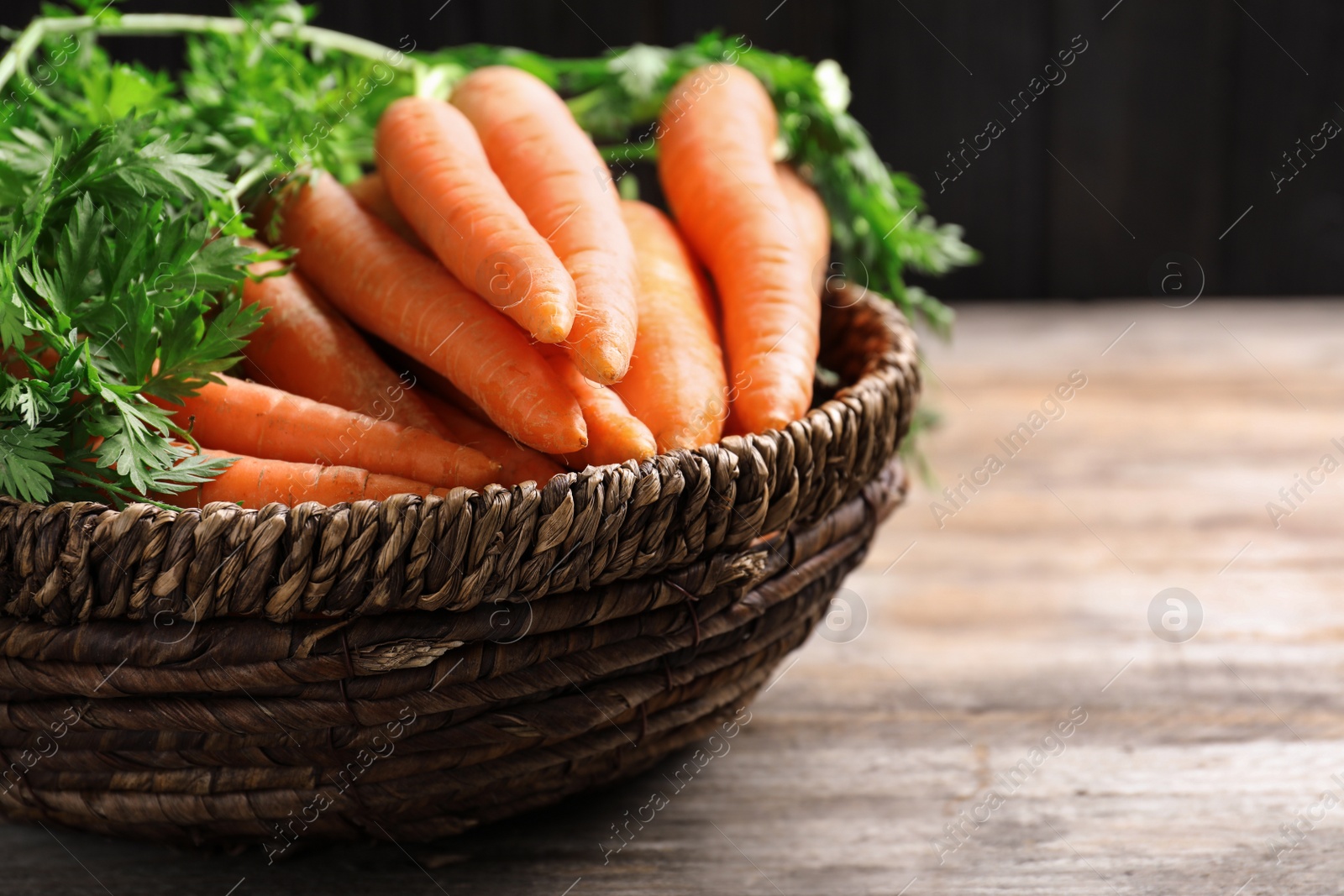 Photo of Basket of carrots on wooden table, closeup