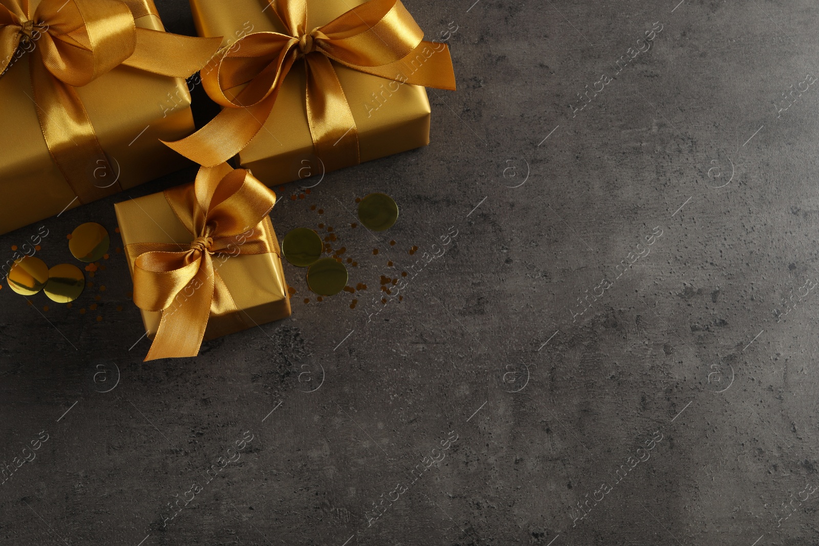 Photo of Three golden gift boxes and confetti on dark background, top view. Space for text