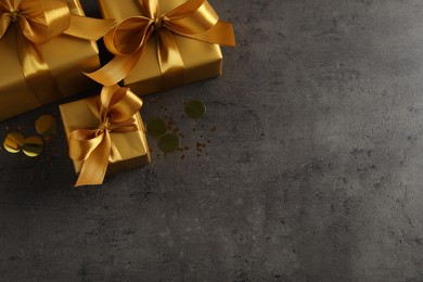 Three golden gift boxes and confetti on dark background, top view. Space for text