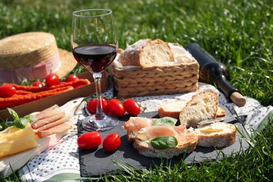 Photo of Blanket with wine and snacks for picnic on green grass