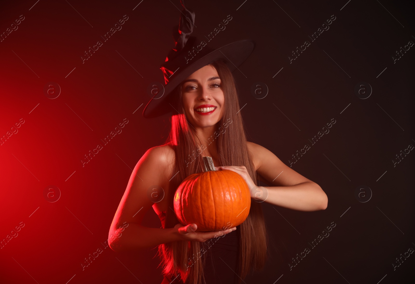 Photo of Young woman wearing witch costume with pumpkin on dark  background. Halloween party