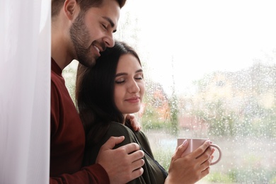 Photo of Happy young couple near window indoors on rainy day