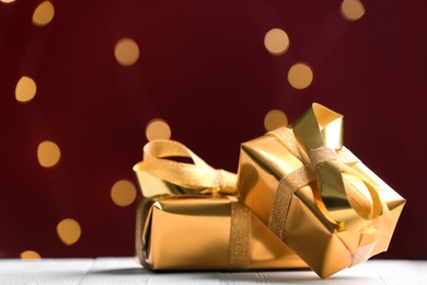 Photo of Golden gift boxes against red background with blurred lights, space for text