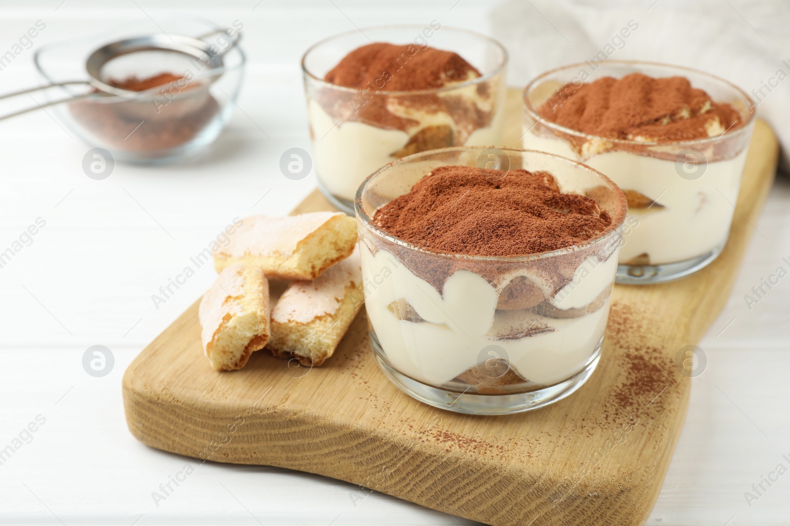 Photo of Delicious tiramisu in glasses and cookies on white table