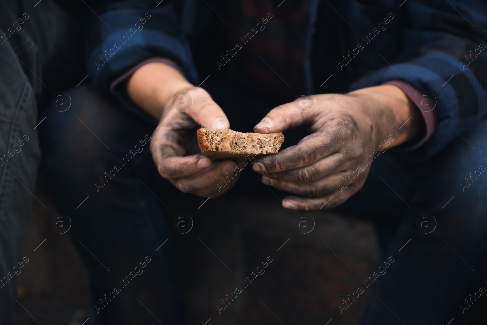 Photo of Poor homeless with piece of bread outdoors, closeup