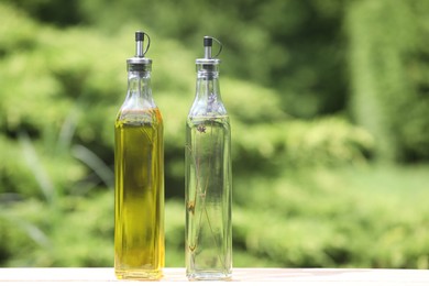 Bottles of healthy cooking oils on wooden table outdoors. Space for text