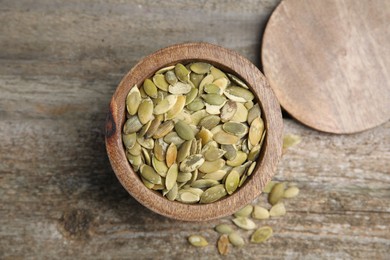 Photo of Dish with pumpkin seeds and lid on wooden table, flat lay