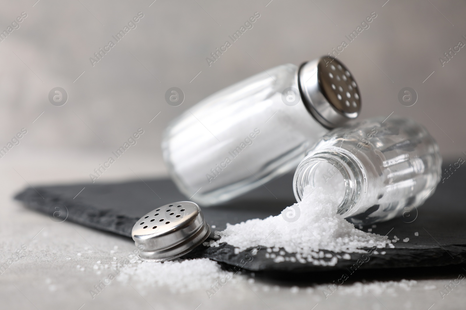 Photo of Natural salt in shakers on grey table, closeup. Space for text