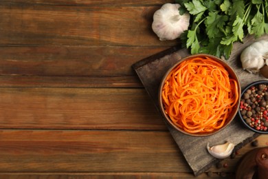 Photo of Delicious Korean carrot salad, garlic, spices and parsley on wooden table, flat lay. Space for text