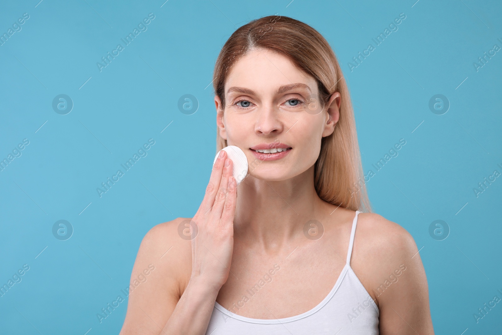 Photo of Beautiful woman removing makeup with cotton pad on light blue background, space for text