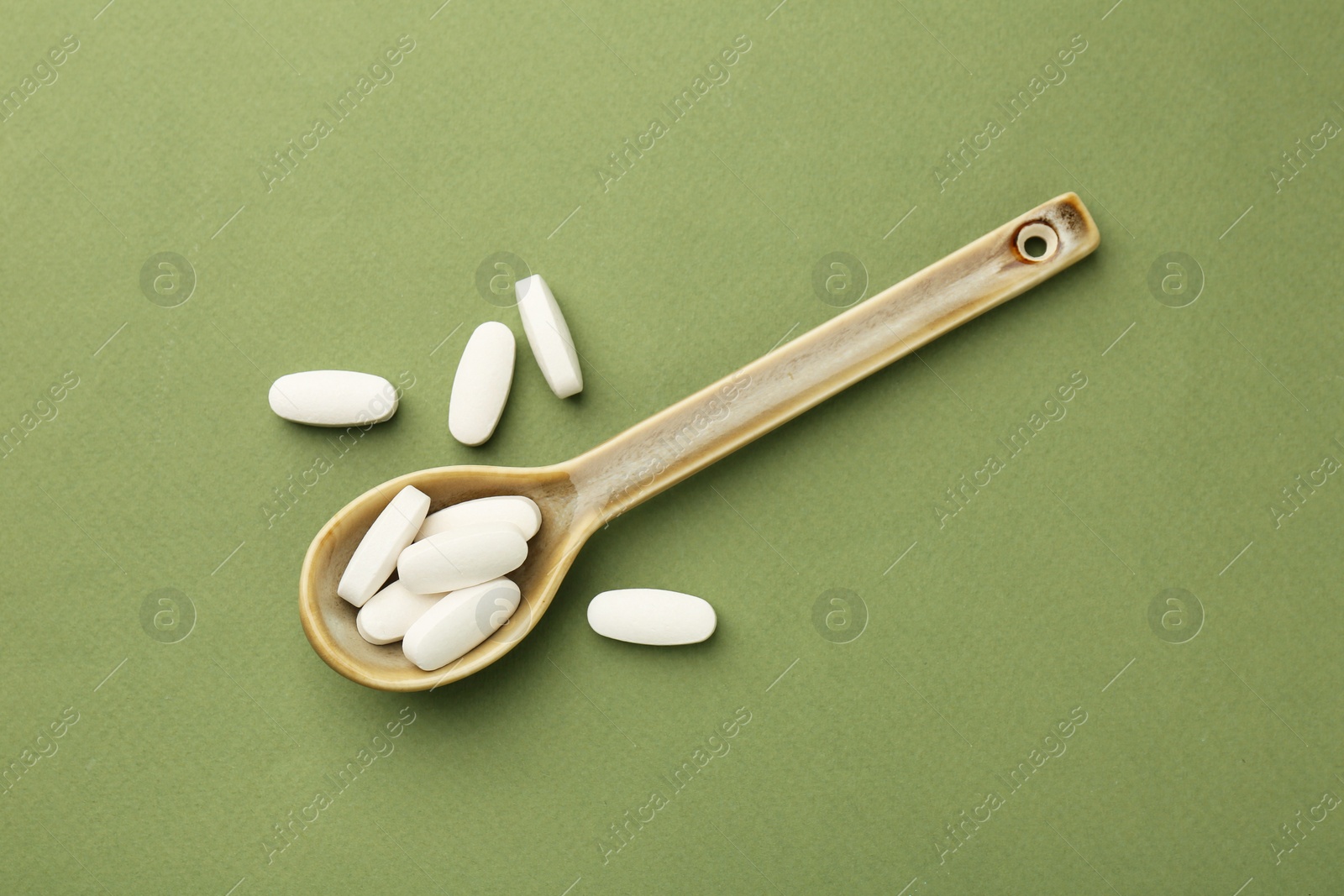 Photo of Vitamin pills in spoon on olive background, top view