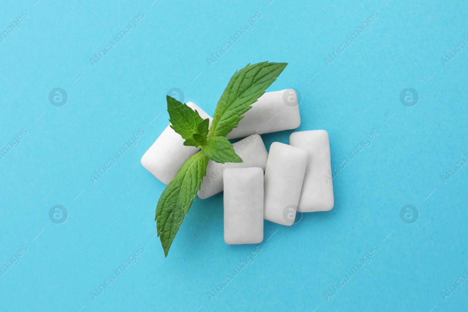 Photo of Tasty white chewing gums and mint leaves on light blue background, top view