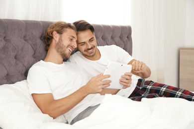 Photo of Happy gay couple with tablet computer on bed at home