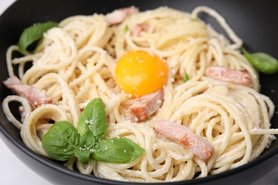 Photo of Delicious pasta Carbonara with egg yolk in black bowl, closeup