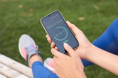 Photo of Young woman using fitness app on smartphone outdoors, closeup